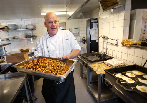 Kocken Crille Olsen i golfrestaurangen på Gagnefs GK står i köket och håller en långpanna med nylagad pytt i panna. På stekbordet bredvid steks det ägg. 