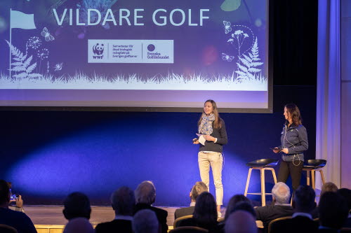 Två kvinnor på scen inför publik. På presentationen bakom syns texten Vildare golf och en samarbetslogga för WWF och Svenska Golfförbundet.