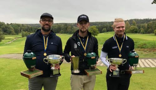Tre män i 25-45-årsåldern står utomhus på en golfbana, hållandes pokaler och medaljer från ett svenskt mästerskap.