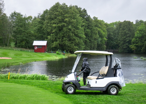 Golfbil, golfspelare och Karlskoga GK:s vattenreserv Valån med pumphuset i bakgrunden. 